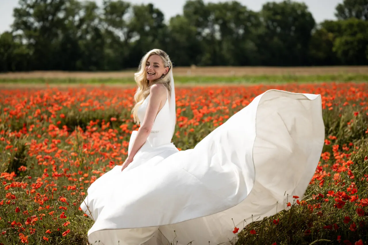 Braut im wehenden Kleid in einem Mohnfeld