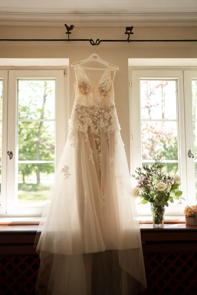 Brautkleid hängt im Gegenlicht vor einem Fenster